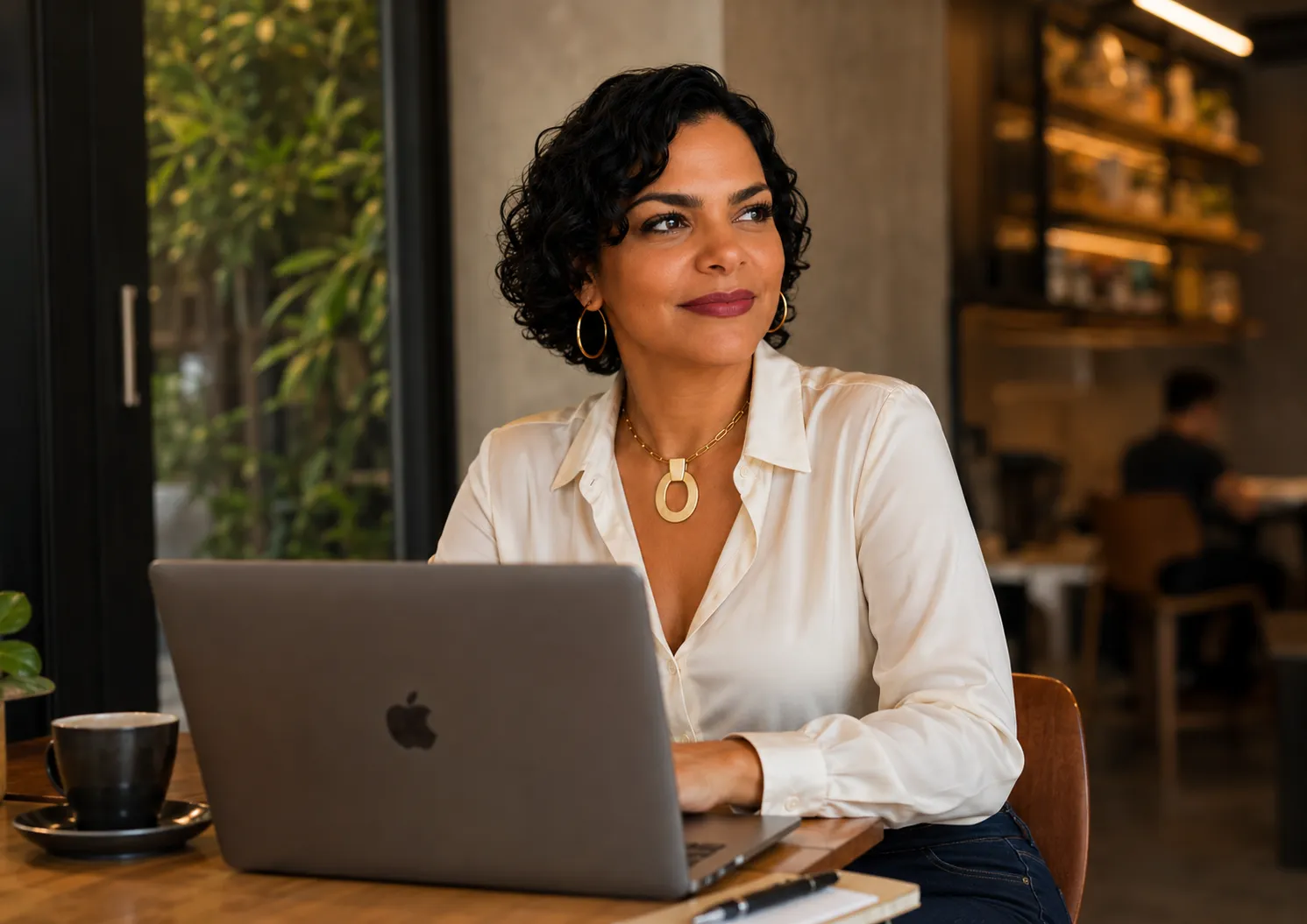 Cynthia Carvalho trabalhando no notebook em um café, com luz natural